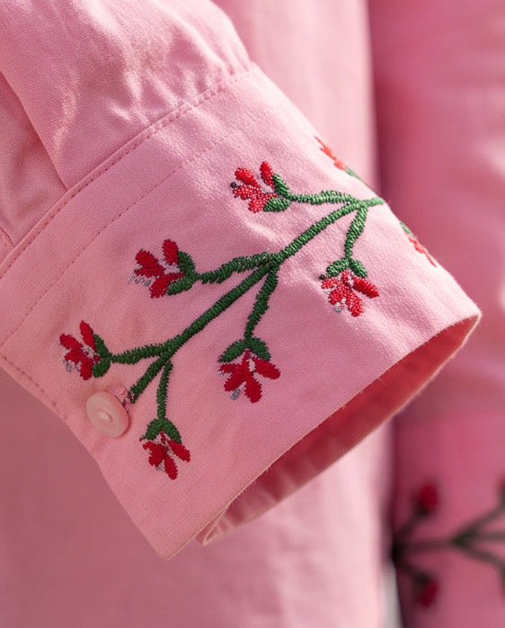 A close-up of a pink long-sleeve button-up shirt with red and green floral embroidery on the cuffs, worn by a model. The brand logo 'RONAO' is visible in the top left corner.