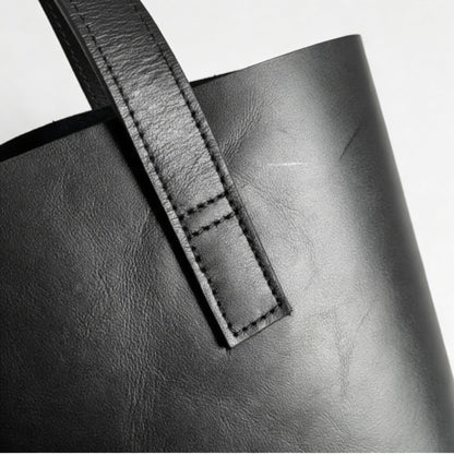 Close-up of a black leather bag with a strap on a white background