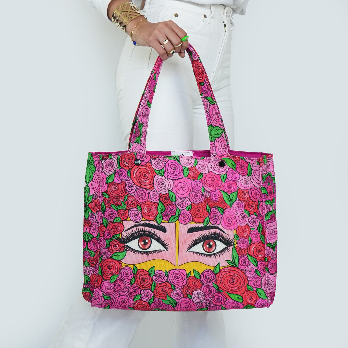 Tote bag with floral design and eye illustration held by a person against a white background