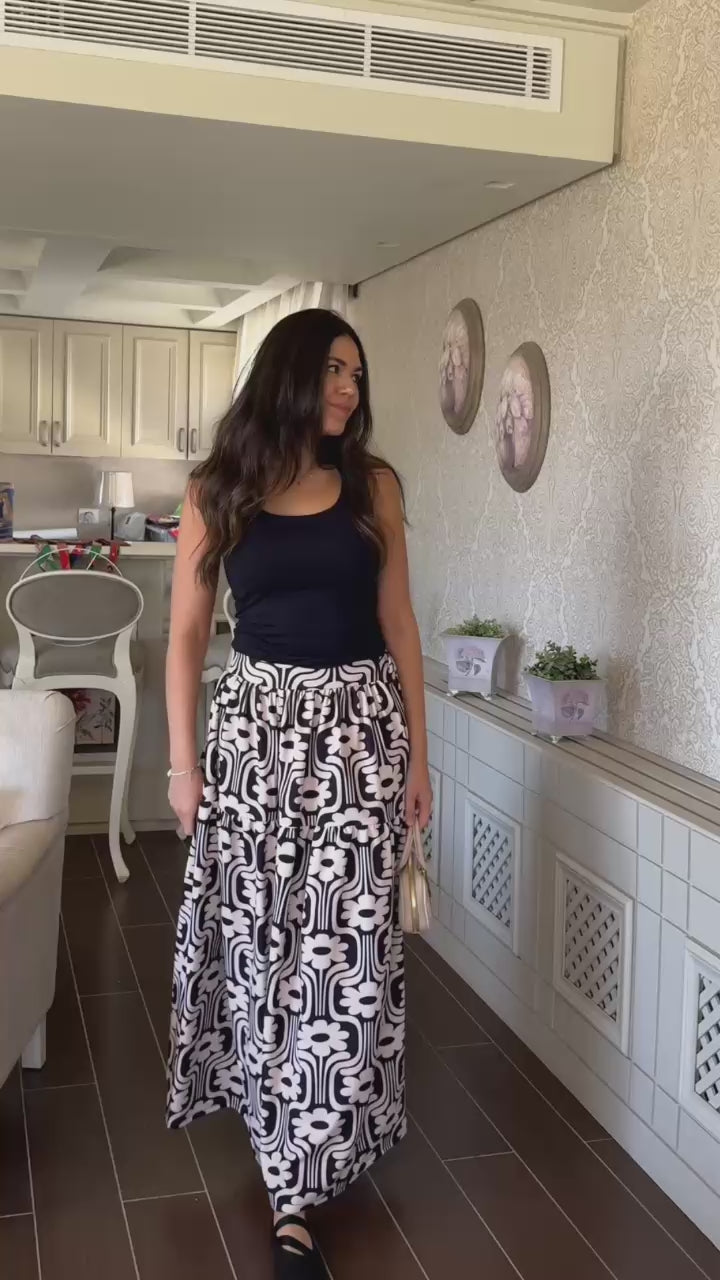 Woman wearing a black top and patterned skirt holding a clutch 