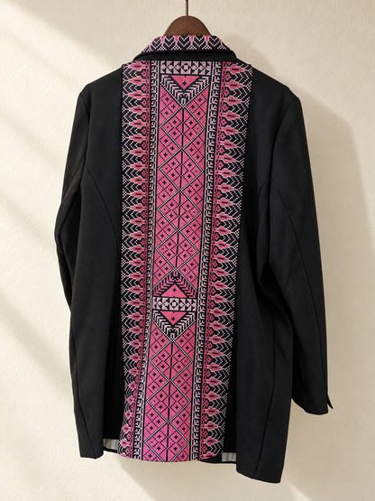 Back view of black blazer with a long pink geometric embroidered panel on a wooden hanger